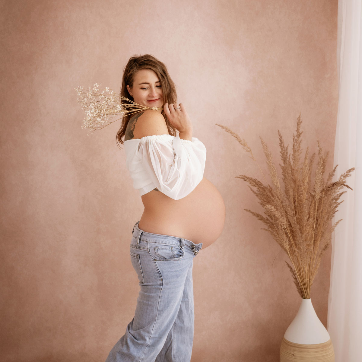 Schwangere Frau mit Trockenblumen zeigt ihren Babybauch im Profil