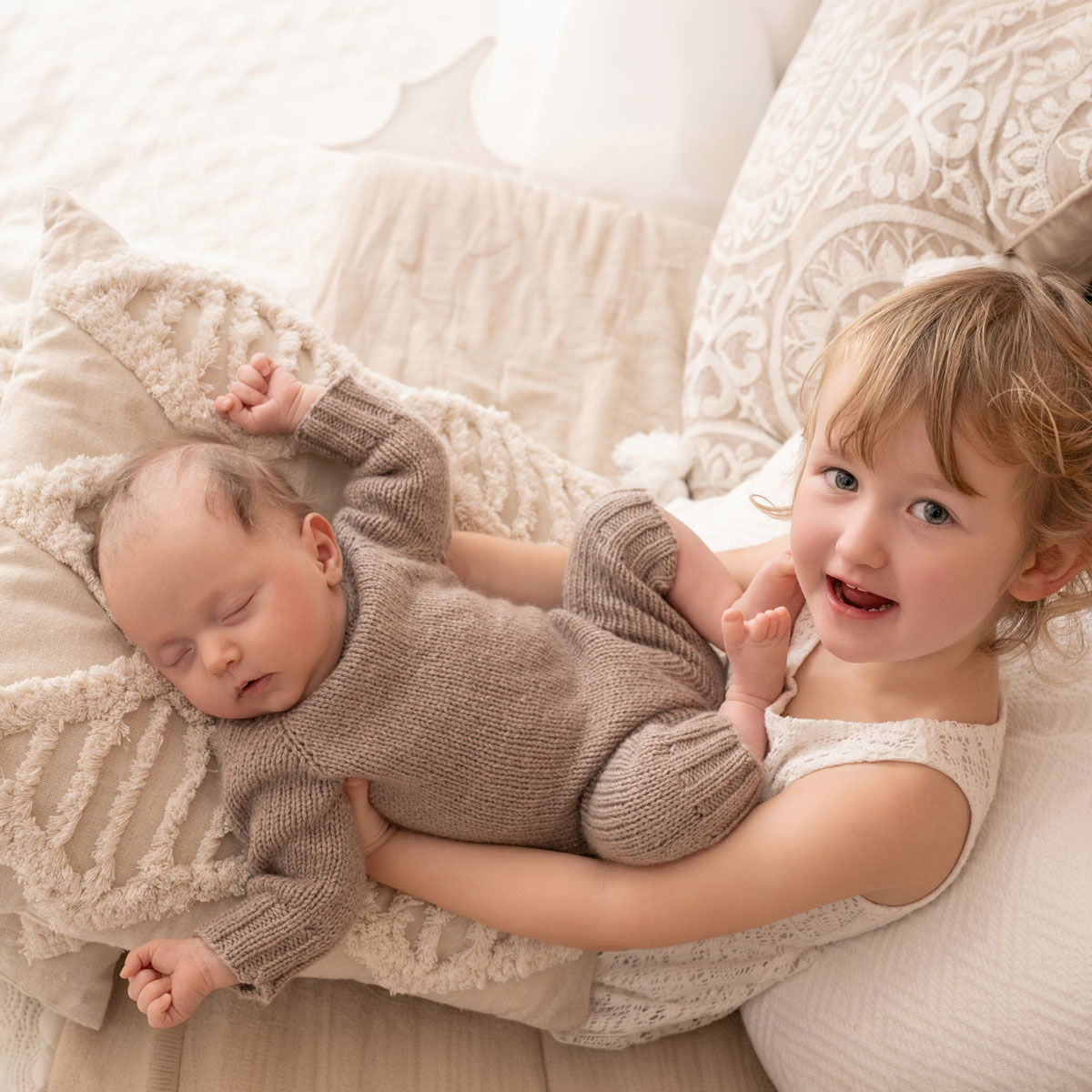 Große Schwester liegt lachend neben dem schlafenden Baby