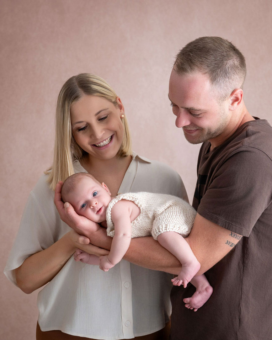 Mama und Papa halten gemeinsam ihr Neugeborenes und schauen es lächelnd an