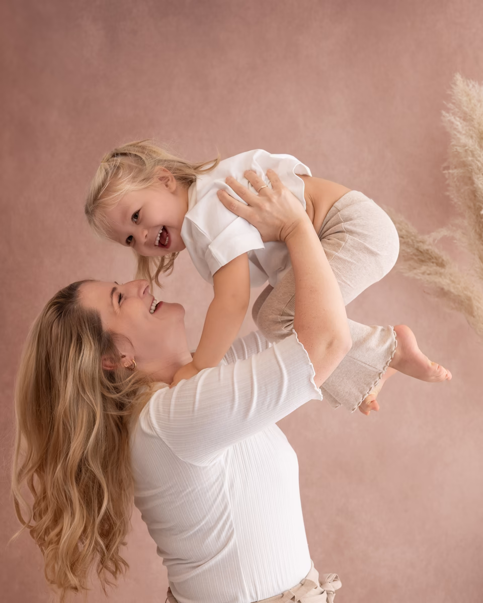 Mama hebt ihr lachendes Kleinkind in die Luft, Familienfotografie im Studio in Pitzenberg