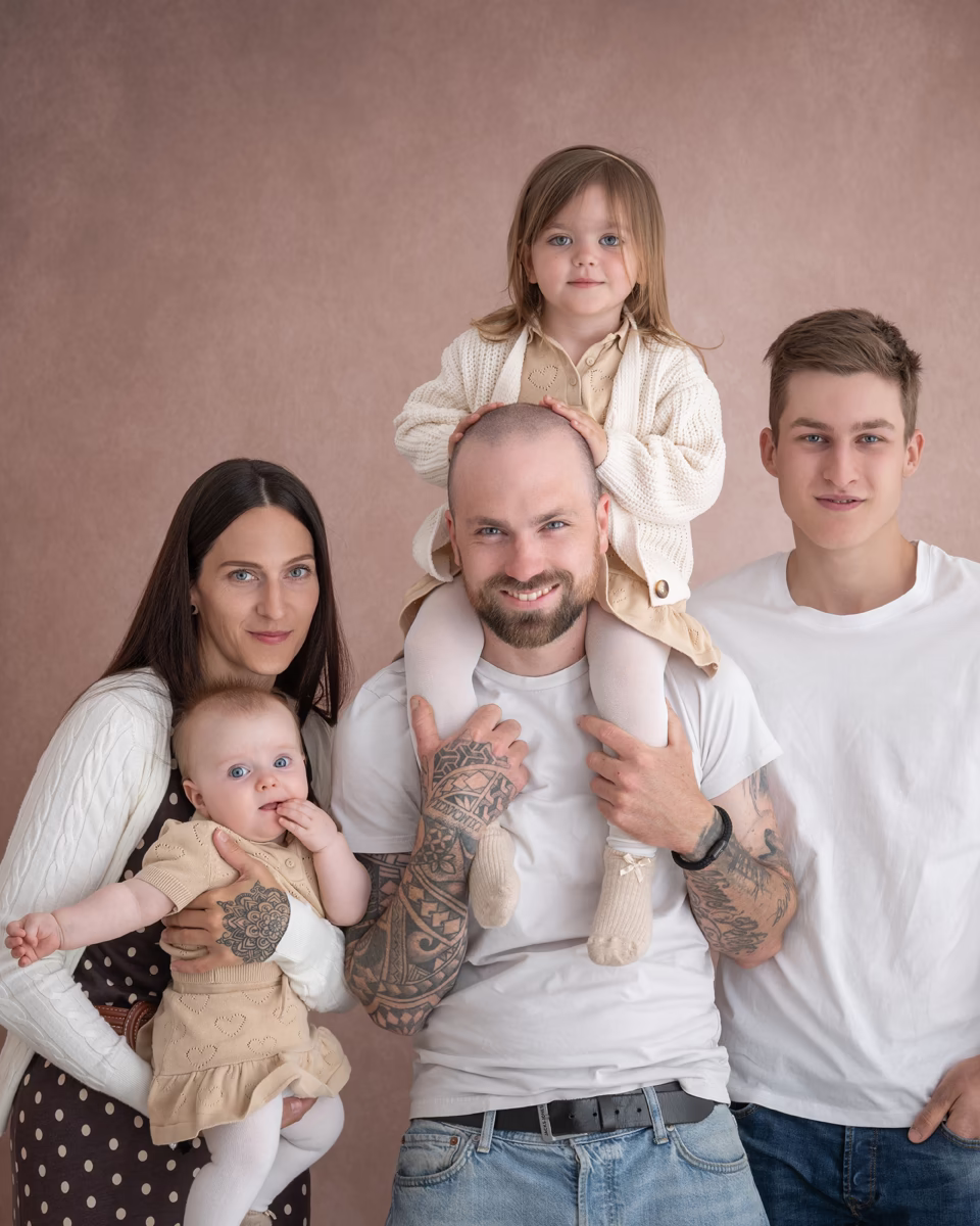 Familie mit drei Kindern im Studio, das Kleinkind sitzt auf Papas Schultern, Mama hält das Baby